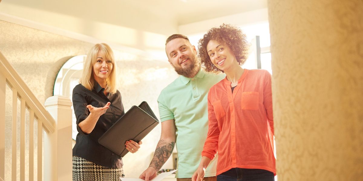 Smiling real estate agent showing a home to a couple standing in a hallway.