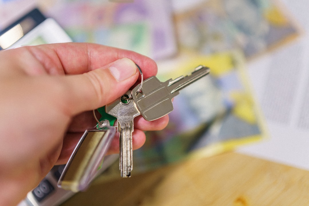 An overhead view of a person's hands using a calculator on a clean desk, with a set of house keys nearby, illustrating the financial decisions involved in choosing a real estate agent.