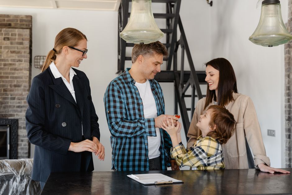 A smiling couple accepts the keys to their new home from a real estate agent, symbolizing the financial success and satisfaction of using a 1% commission model.
