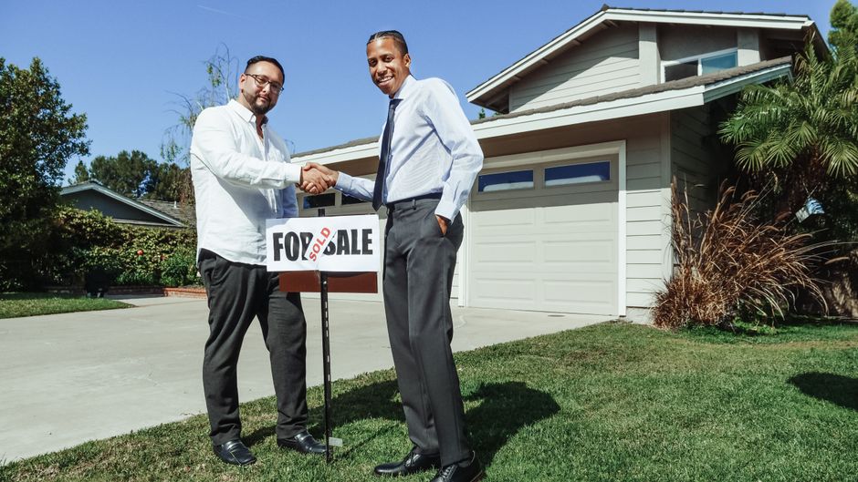 A beautiful modern suburban home with a 'For Sale' sign in the manicured front yard on a bright, sunny day, representing a fast and successful home sale.