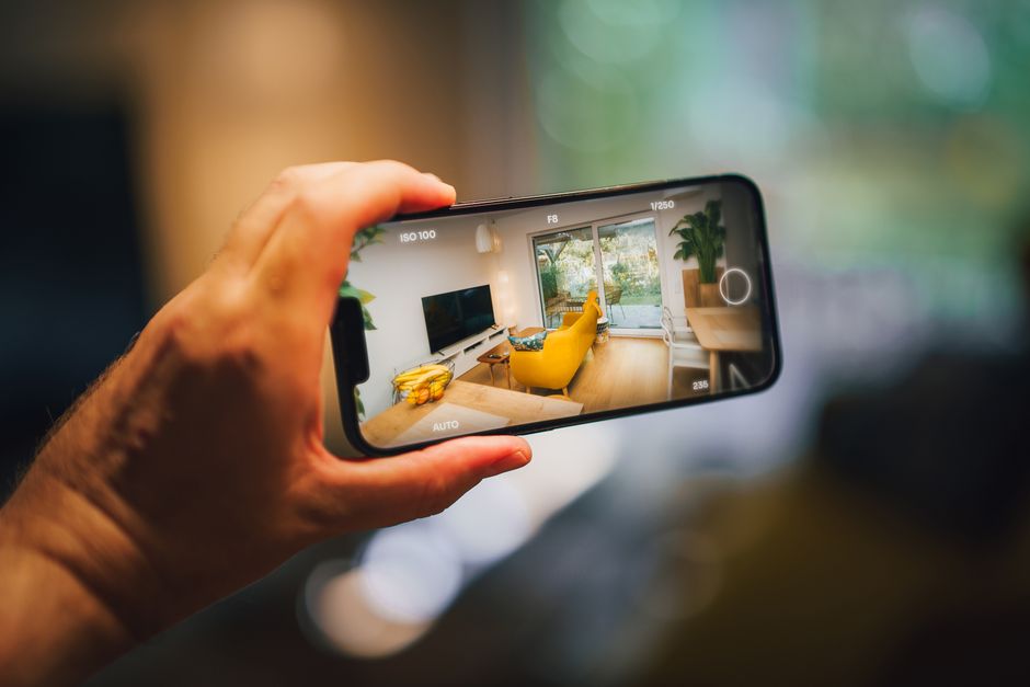 A close-up of a person's hands holding a smartphone, browsing a clean, modern real estate website with high-quality photos of homes for sale.