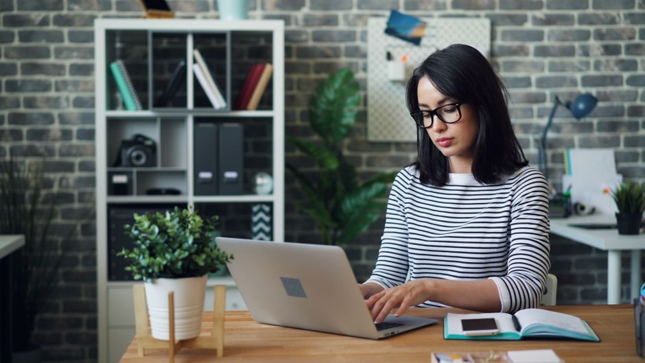 A professional and friendly host smiles while working on a laptop in a bright, modern living room, representing the control and profitability of a direct-booking business.
